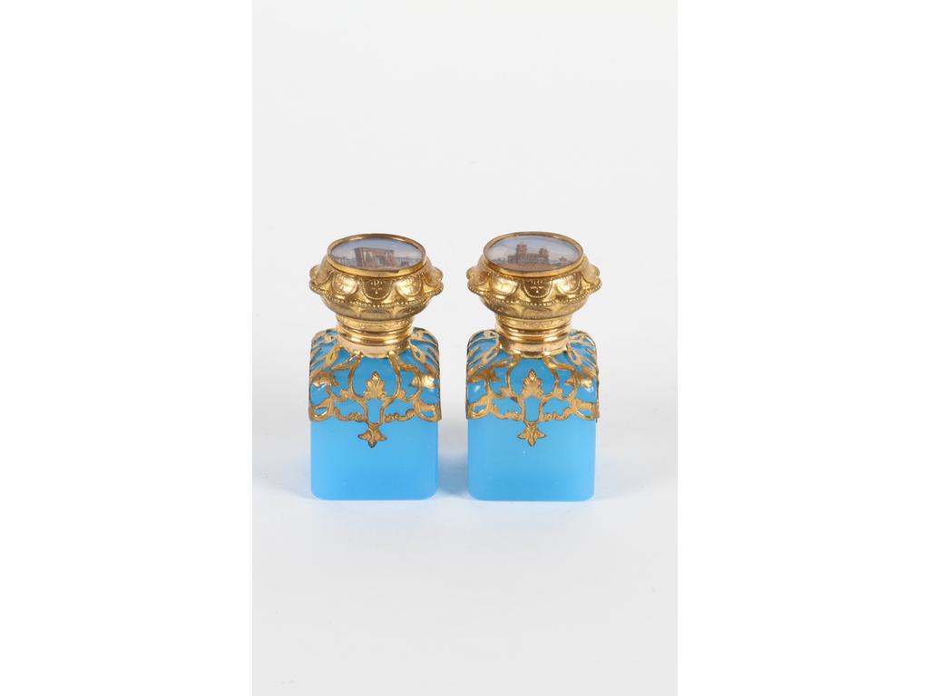 Paire de petits flacons en opaline bleu turquoise ornés d'une monture en laiton et tôle dorée. Les bouchons à décor de lithographies représentant la cathédrale Saint Sulpice et la porte Saint Denis. Bon état. (Manques un petit bouchon en verre sous un couvercle). Hauteur : 6.5 cm
