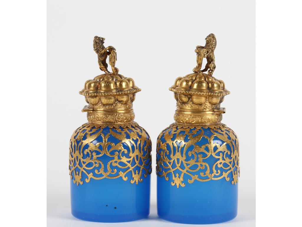 Paire de flacons à thé en opaline bleue, ornés d'une monture en laiton et tôle dorée. Les couvercles à décor de lions tenant des cartouches. Bon état. Hauteur : 15 cm.