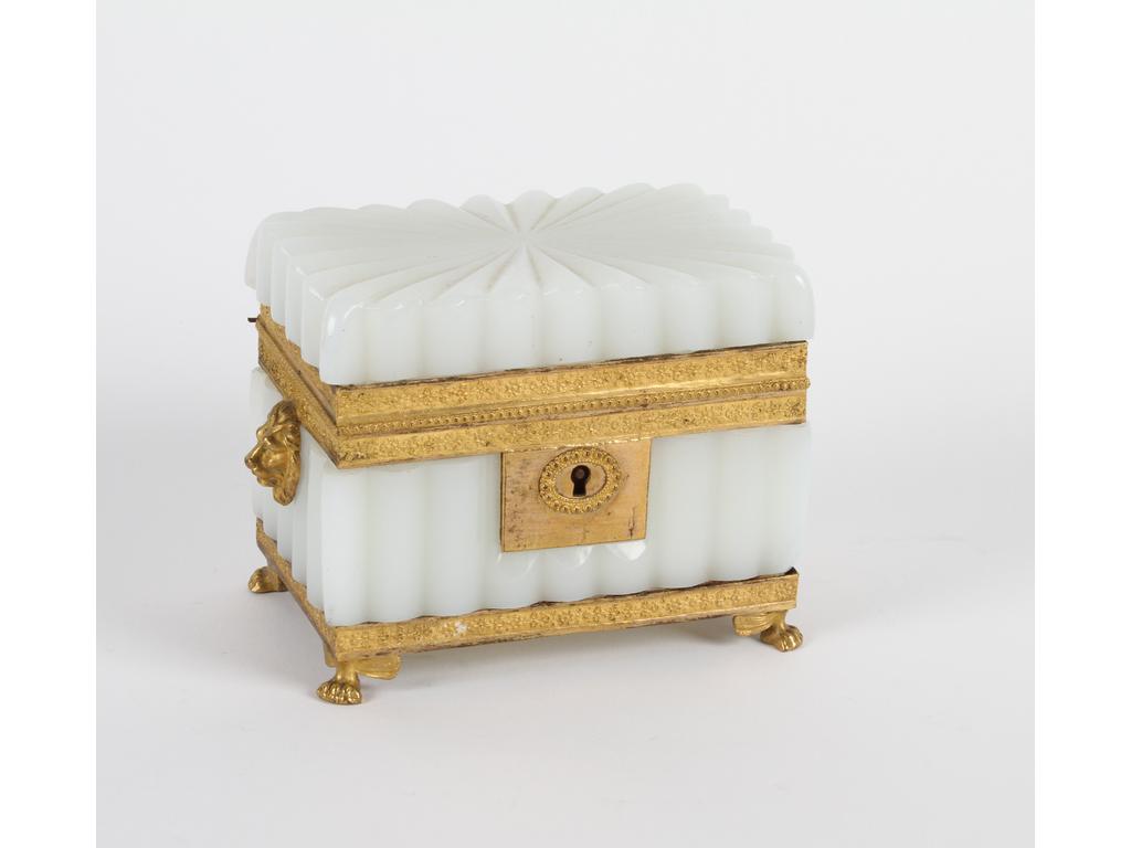 Coffret en opaline blanche côtelée sur une monture en laiton et tôle dorée, ornée de deux mufles de lion sur les côtés. (Un éclat d'opaline sous le coffret et sans clé). Hauteur : 9 cm.