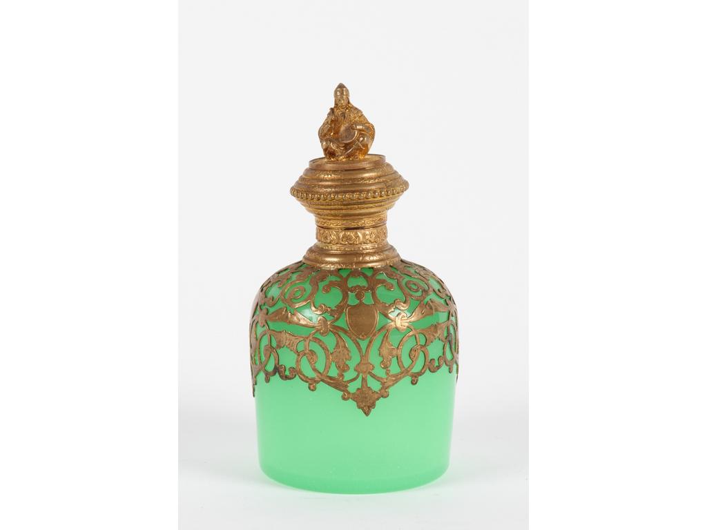 Flacon en opaline verte sur une monture en laiton et tôle dorée, le bouchon orné d'un personnage persan assis en tailleur. Bon état. Hauteur : 13 cm.