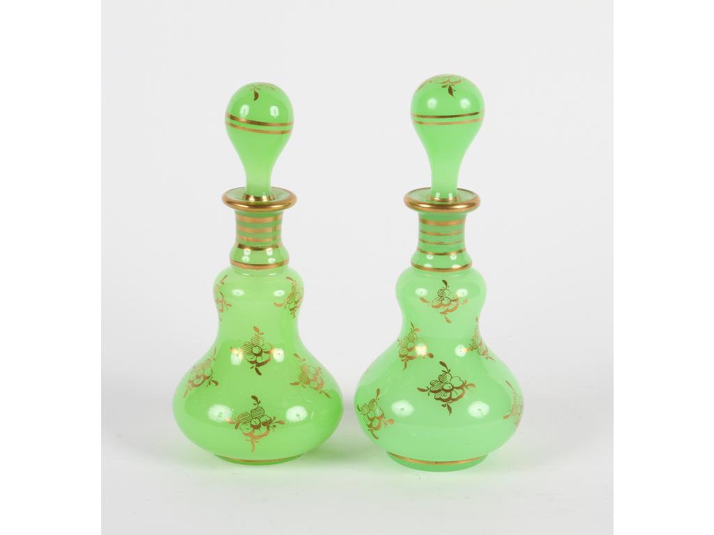 Paire de flacons piriformes en opaline verte à décor de fleurs et liserés dorés. (Eclats et chocs sur les bouchons au niveau des cols). Hauteur : 18 cm