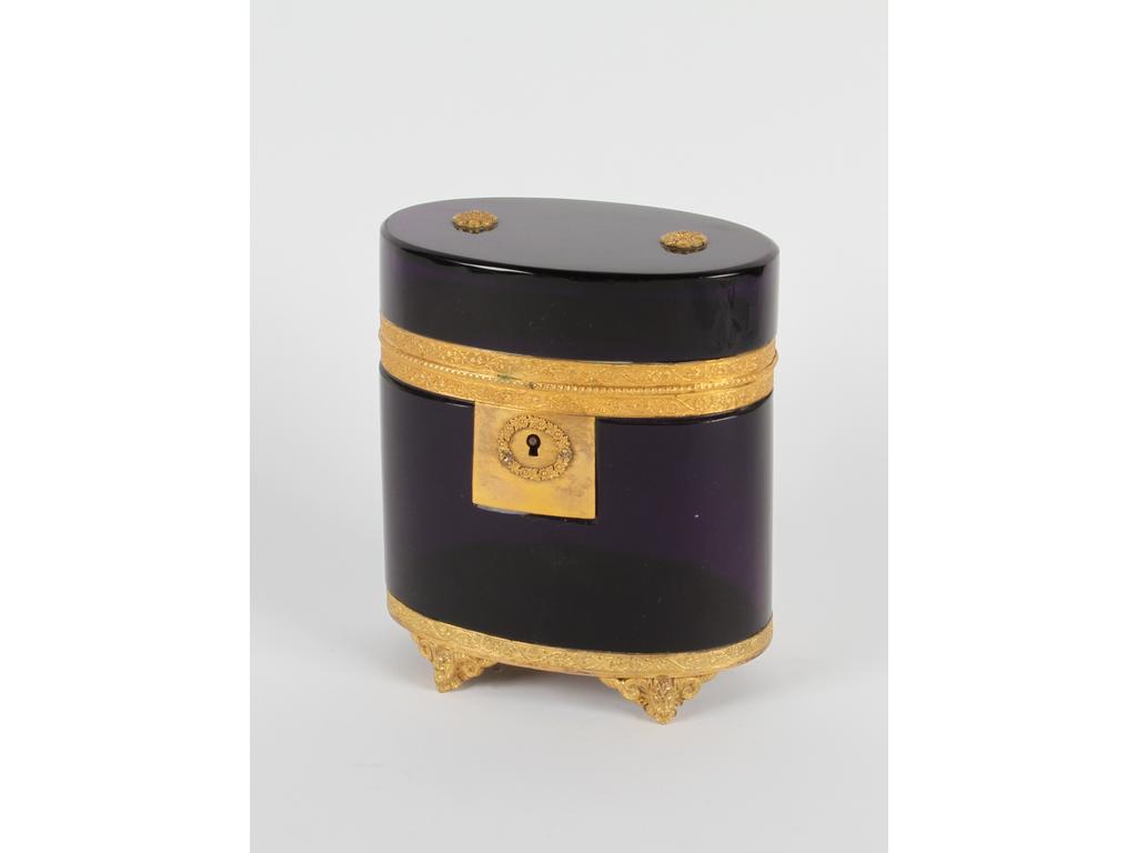 Coffret de forme ovale en opaline couleur améthyste, sur une monture en laiton et tôle dorée. Le couvercle orné de deux petites fleurs. Hauteur : 14 cm. (Bon état, sans clé)