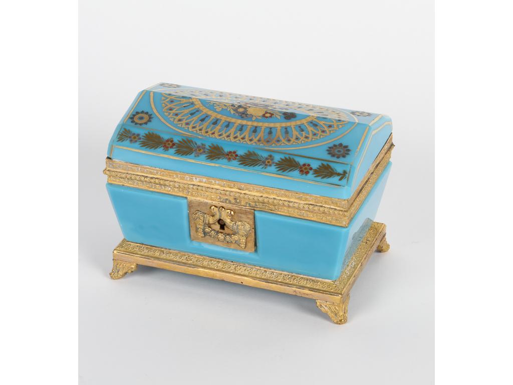 Coffret de forme sarcophage en opaline bleu turquoise sur une monture en laiton et tôle dorée. Le couvercle à décor peint et doré. (Bon état général, traces de plâtre sur la monture, sans clé). Hauteur : 9 cm. Longueur : 13 cm.