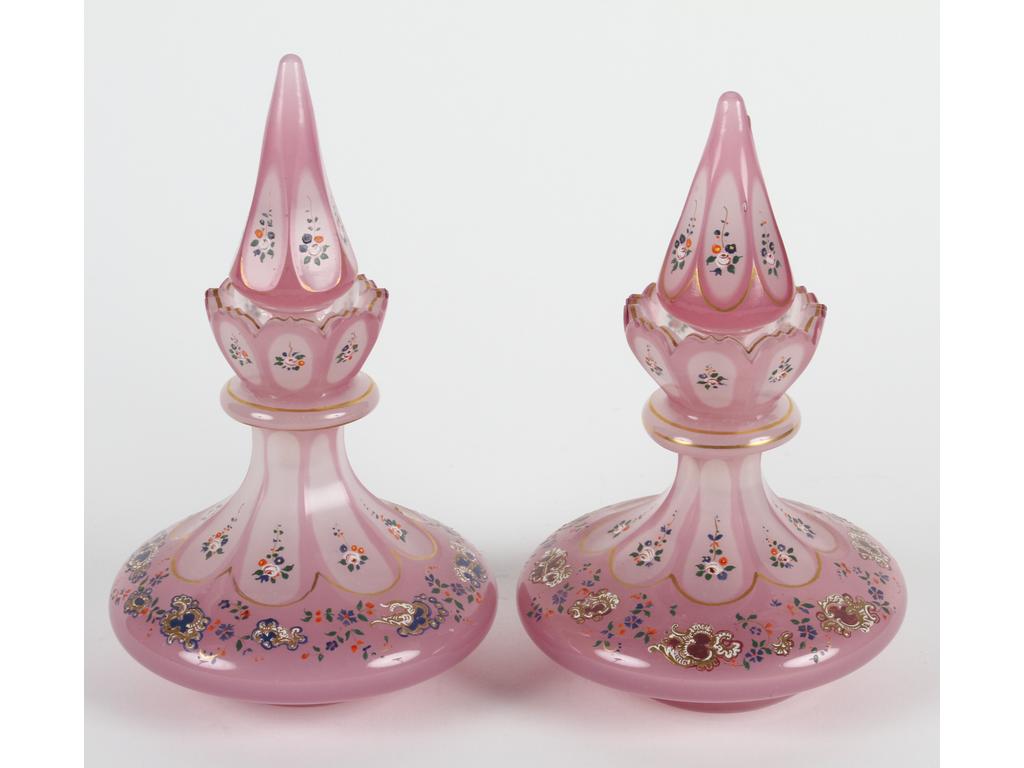 Paire de flacons en opaline blanche doublée rose et taillée. Décor émaillé et peint de rocailles et fleurettes. (Bon état général, défauts sur les cols). Hauteur : 20 cm.
