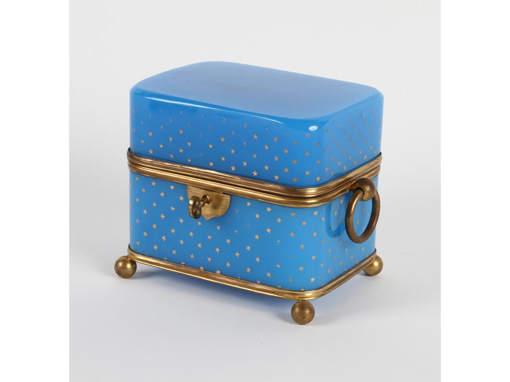 Coffret à senteurs en opaline bleue à décor d'un semis d'étoiles dorées avec une monture en laiton et tôle dorée. A l'intérieur, six petits flacons en verre et bouchon en laiton (manque deux petits bouchons en verre) avec une clé. Décor d'étoiles dorées sur le couvercle entièrement effacé. Hauteur : 14 cm.