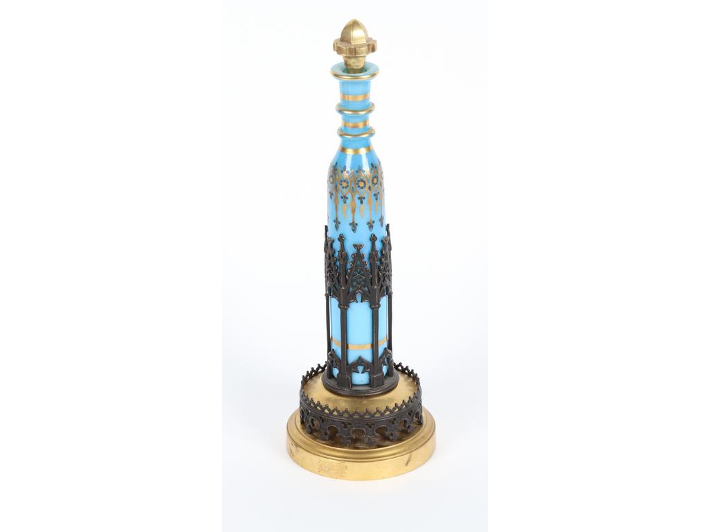 Long flacon en opaline bleue en forme de bouteille. Décor doré et monture en laiton et métal noir de style gothique. (Monture à refixer sur pas de vis). Hauteur : 33 cm. Bon état.