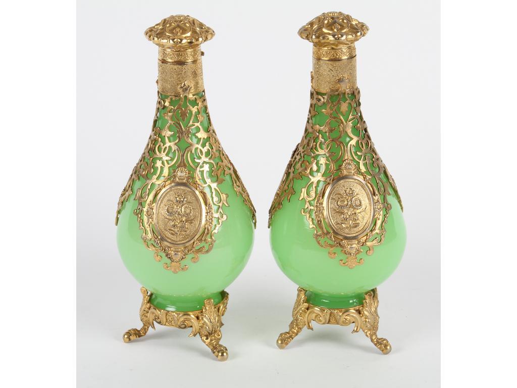 Paire de flacons en opaline verte ornés d'une monture ajourée en laiton et tôle dorée à décor de médaillons fleuris. Hauteur : 20 cm. Bon état (manque les petits bouchons en verre sous les couvercles)