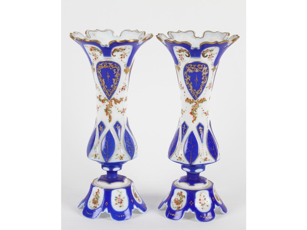 Paire de vases diabolos en opaline blanche doublée bleu et taillée. Décor peint et émaillé de fleurs et d'écussons. (Deux éclats avec manques sur un socle, infimes éclats aux cols)