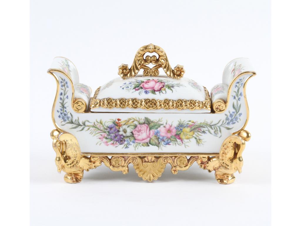 PARIS, Jacob PETIT : Encrier en forme de lit de repos en porcelaine blanche et dorée à décor peint de fleurs. Les pieds en forme de cygnes. Marqués J.P. (Bon état général). Longueur : 20 cm.