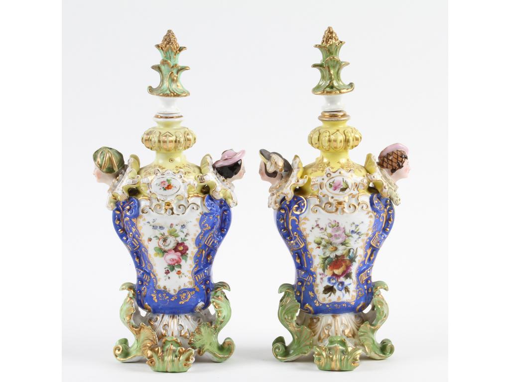 PARIS, Jacob PETIT : Paire de flacons à parfum en porcelaine très richement peints et ornés de deux têtes de part et d'autre. (Un vase avec têtes et socle restaurés). Marqués J.P pour les deux. Hauteur : 27 cm.