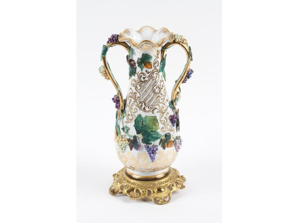 Vase à anses en porcelaine blanche à décor doré de rinceaux. Les anses et le corps ornés en relief de pampres et grappes de raisins. (Une anse cassée et recollée.). Sur une monture en bronze doré. Hauteur : 32 cm.