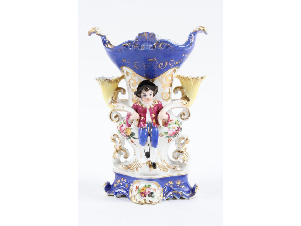 PARIS, Jacob PETIT : Petit vase en porcelaine blanche richement peint et doré sur fond bleu, orné de deux personnages tenant deux cornes pique-fleurs. Marqué J.P. (Une petite corolle jaune restaurée). Hauteur : 19 cm.