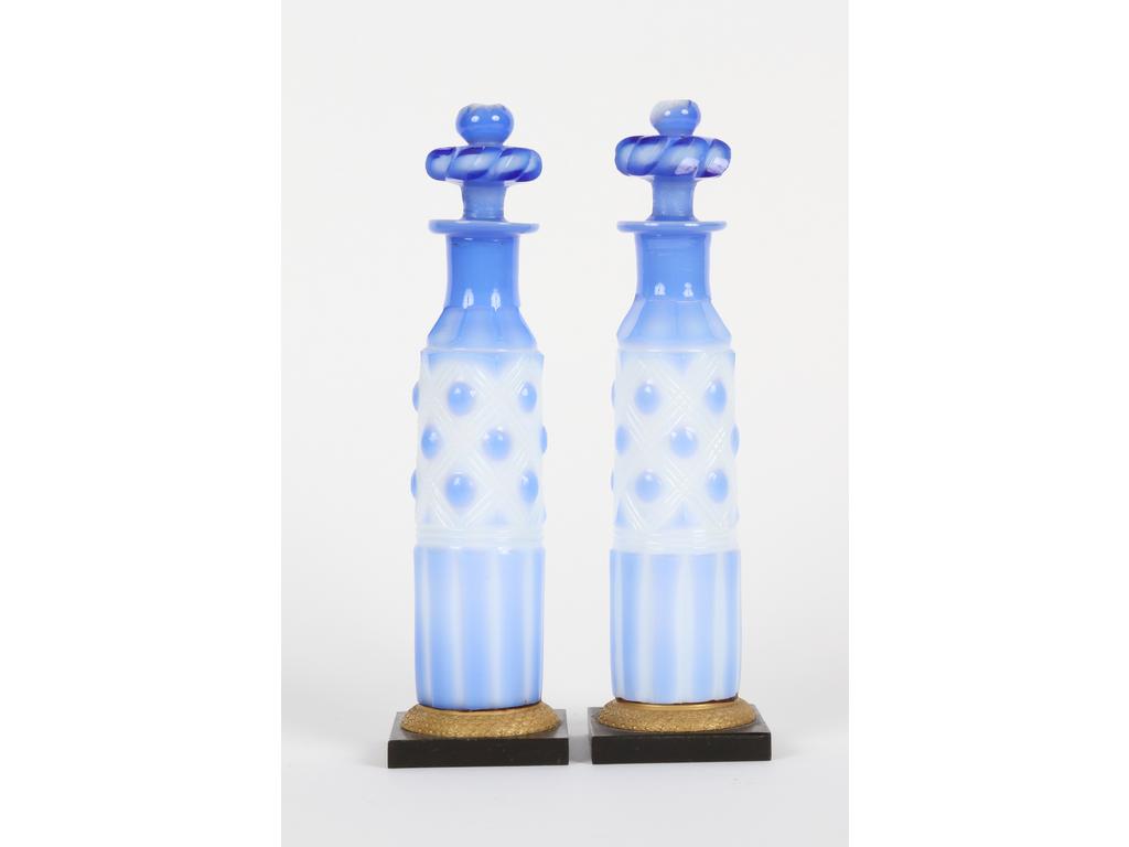 Paire de flacons en forme de bouteilles en opaline blanche doublée bleue et taillée. Ils reposent sur un socle en bronze patiné noir avec bague en laiton. (Bon état, infimes éclats aux bouchons). Hauteur :19 cm