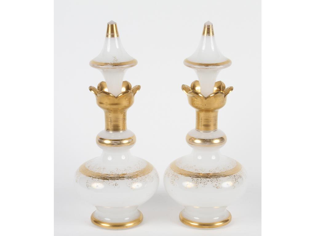 Paire de flacons en opaline blanche à cols et à décor dorés. Bouchons en formes de toupies. (Bon état général, usures à la dorure). Hauteur : 29 cm.
