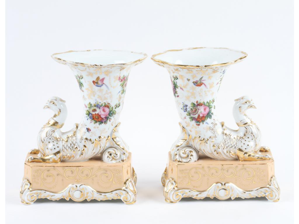 PARIS : Paire de vases rhytons en porcelaine blanche à décor peint de fleurs et têtes de griffons. Les socles couleur peau de pêche. Hauteur : 27 cm. (Bon état)