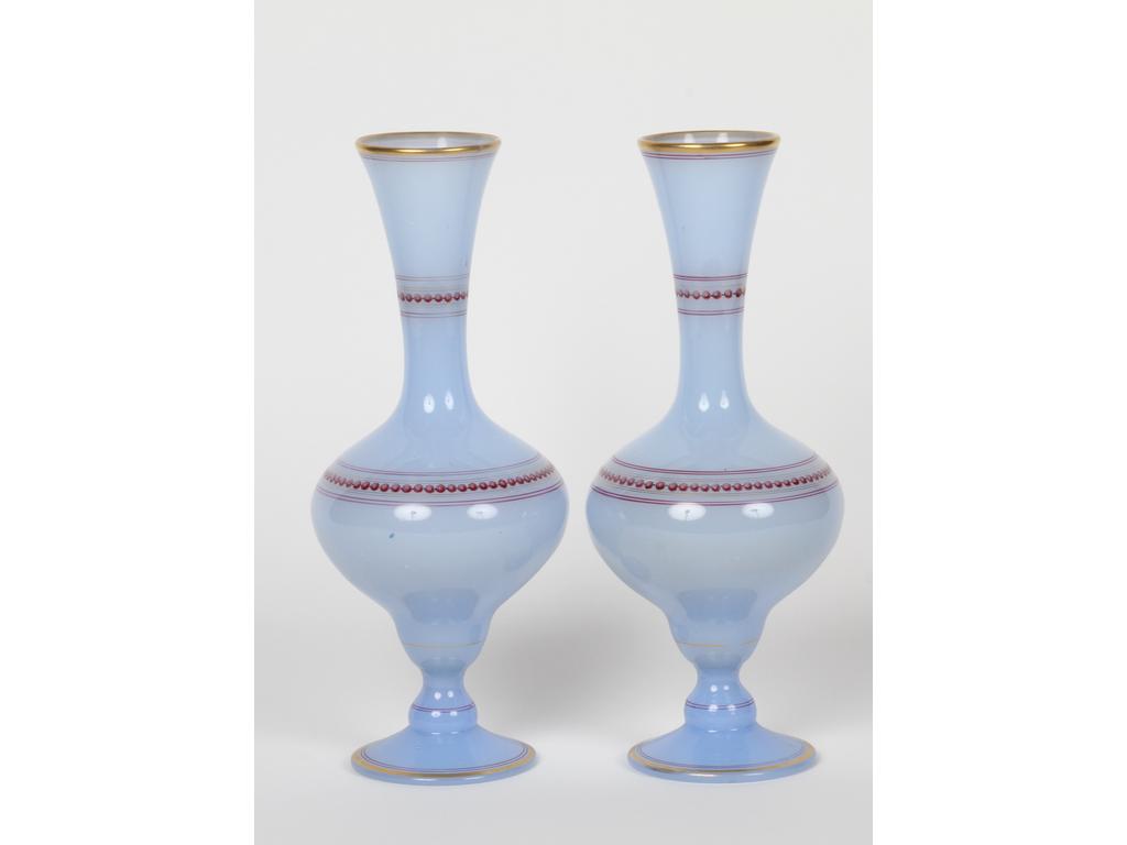 Paire de vases balustres sur piédouche en opaline bleu lavande pâle à décor peint de rais de perles et liserés dorés. (Légères usures à la dorure). Hauteur : 27 cm.