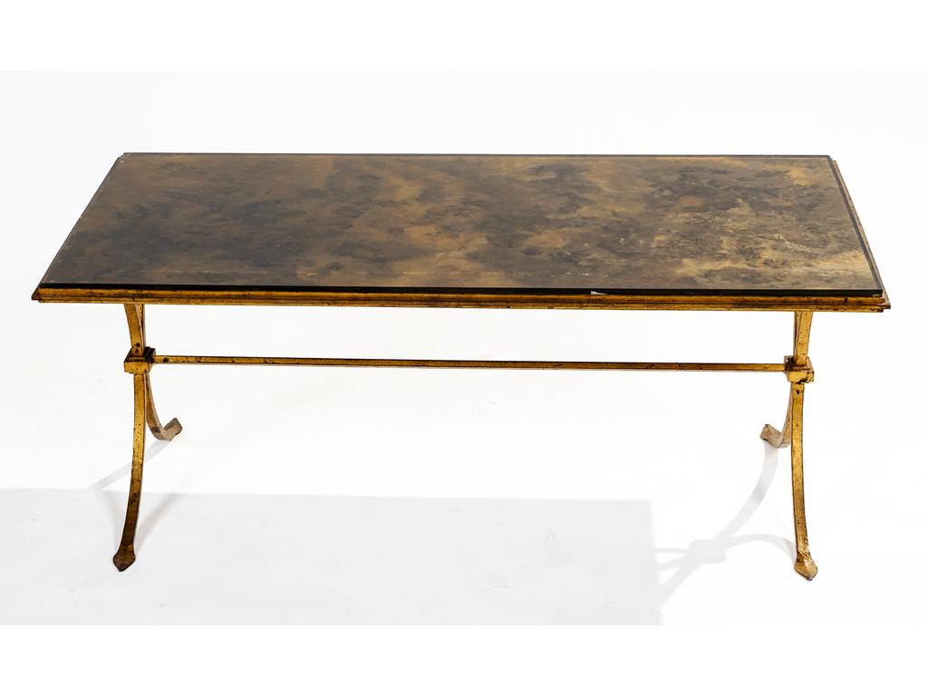 Table basse rectangulaire en fer doré. Plateau en verre églomisé à motif mordoré. Dimensions : 41 x 101 x 51 cm. (Infimes rayures et infime éclat à un angle du verre)