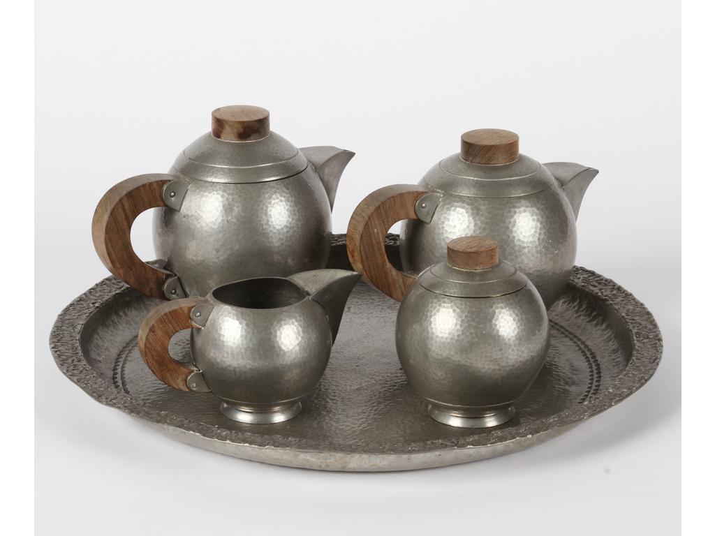 René DELAVAN (1926-1958) : Service à thé et à café en étain martelé. Fretels et poignées en bois comprenant : quatre pièces de formes présentées sur un plateau rond. Epoque 1930. Signés. (Infimes chocs). Diamètre du plateau : 41 cm.