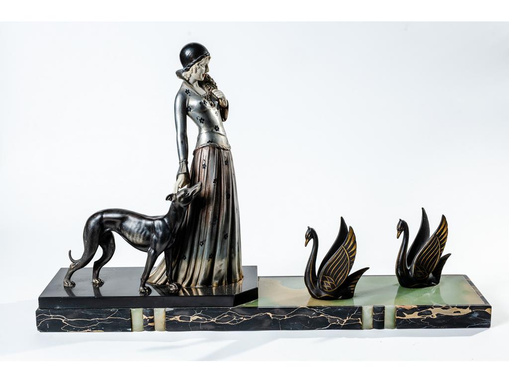 Groupe en régule patiné et argenté représentant une élégante avec un lévrier devant un couple de cygnes. Socle en marbre et onyx. Epoque Art Déco. Hauteur : 46 cm, longueur : 73 cm