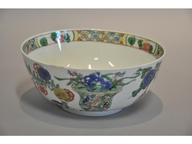 CHINE - KANGXI : Bol en porcelaine blanche à décor peint en polychromie d'arbustes, de barrières, de cahe-pots, de cage à oiseaux et d'un chat.  Intérieur du bassin à décor peint d'un brûle-parfum.  Marque au vase Jue.  Diamètre : 21.5 cm.  Hauteur : 9 cm. Bon état.