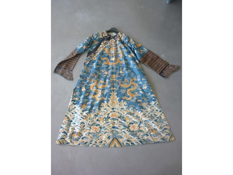 CHINE - XIXe siècle : Robe en soie bleu brodée aux fils dorés et polychromes de neuf dragons à quatre griffes, figurés de face ou de profil, parmi des nuages et fleurs stylisés au-dessus d'une bande de lishui, pivoines, les huit symboles de bonne augure (Ashtamangala, Ba bao en chinois) et des pics
