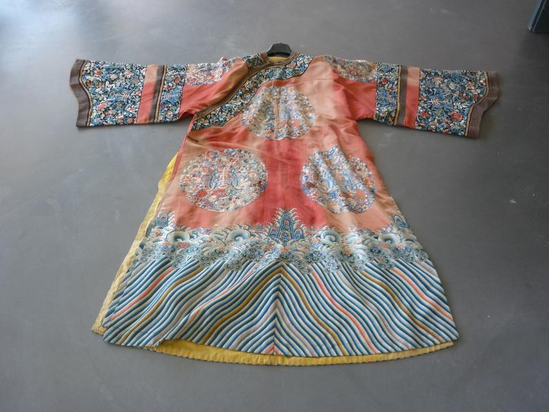 CHINE - XIXe siècle : Robe de femme en soie corail, à décor brodé aux fils polychromes de médaillons des caractères 