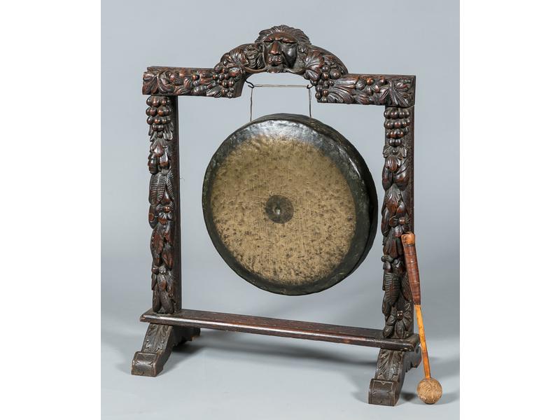 Gong tibétain, disque en laiton fixé sur un encadrement en bois sculpté à décor de mufle de lion et guirlandes de fruits. Diamètre du disque : 55 cm, hauteur totale : 99 cm.