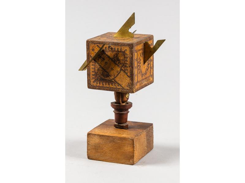 Petit cadran solaire en chêne de forme cubique orné de papier gravé et d'ailerons en laiton.  Signé D. BERINGER.  Socle non d'origine, rapporté.  Hauteur totale : 20 cm.  Dim. côté du cube : 6.5 cm.