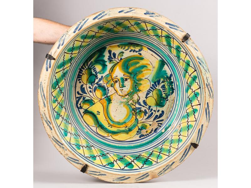 PORTUGAL : Grand plat en terre cuite vernissée à décor d'un personnage en buste et rinceaux feuillagé polychrome. XVIIIe siècle. Diam.: 70cm, H.: 17cm