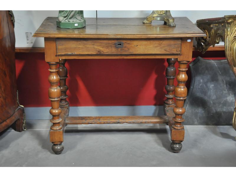 Table à écrire d'époque Louis XIII en noyer et bois naturel, plateau rectangulaire ouvrant par un tiroir en ceinture, reposant sur quatre pieds balustres en bois tourné reliés par une entretoise en H.  Dim.: 81x100x56 cm. (petites restaurations d'usage)