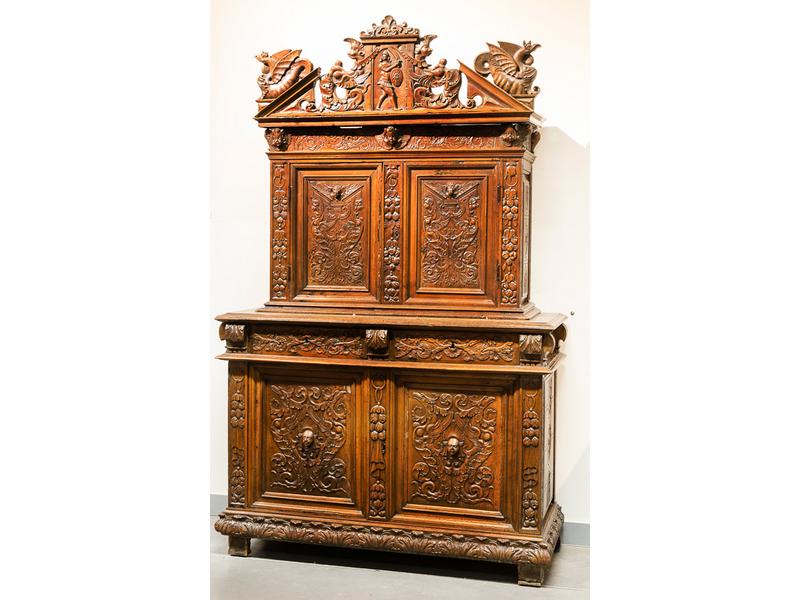 Buffet à deux corps en retrait en noyer ouvrant par quatre vantaux et deux tiroirs en ceinture. Riche décor sculpté de mascarons d'indiens et d'anges, de fruits, de rinceaux feuillagés, surmonté d'un fronton traingulaire brisé orné de chimères. Début XVIIe siècle. Dim.: 220x137x53 cm. (les dragons l