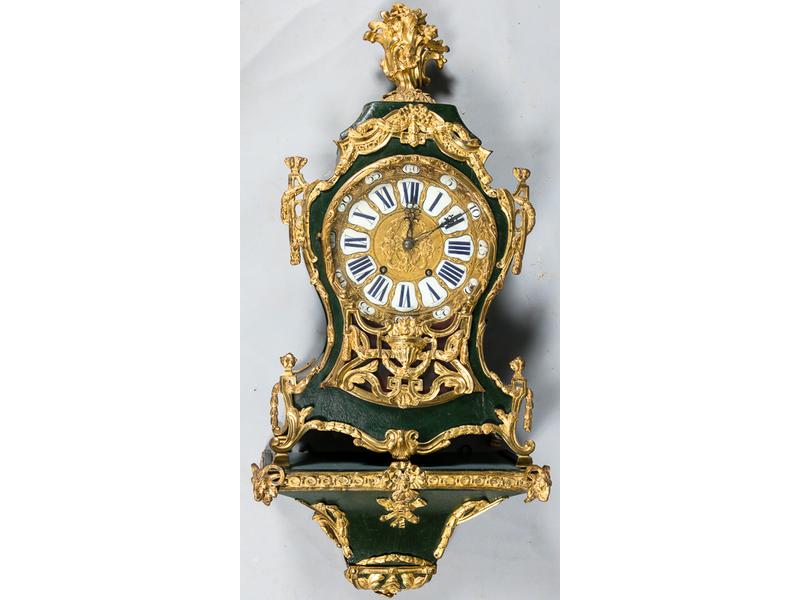 Cartel d'applique en bois laqué, bronze et laiton doré présentant un riche cadran à décor repoussé d'un personnage en buste et têtes de dauphin et cartouches émaillés à chiffres romains.  Mouvement à fil, signé Chaux de Fond.  Sonne les heures, les demi-heures et les quarts.  Présente une corbeille