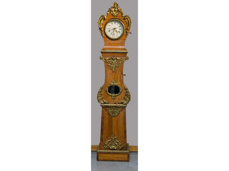 Régulateur de parquet en placage de bois de rose à riche ornementation de bronzes et laiton dorés à décor de cartouches, palmettes et rinceaux feuillagés.  Cadran émaillé blanc à chiffres romains signé Hubert au Mans.  Epoque Louis XV.  Dim.: 230x49x30 cm. (mouvement remplacé, modifications et resta