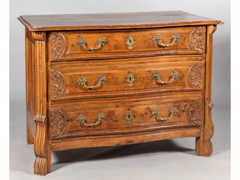 Commode mazarine en noyer mouluré et sculpté de rocailles.  Façade galbée ouvrant par trois tiroirs.  Plateau naturel reposant sur des montants moulurés et stylisés.  Entrées de serrures et poignées en bronze.  Epoque début XVIIIe siècle.  Dim.: 94x131x94 cm. (fond et intérieurs des tiroirs restauré