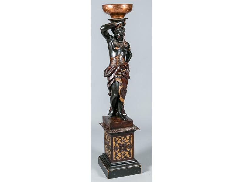 Porte-torchère en bois sculpté et laqué représentant une jeune nubienne déhanchée porteuse d'eau vêtue d'un pagne.  Venise.  Fin XIXe siècle.  Hauteur : 120 cm.  Elle est présentée reposant sur un socle gaine en bois sculpté (55 cm).  Vasque en laiton rapportée.