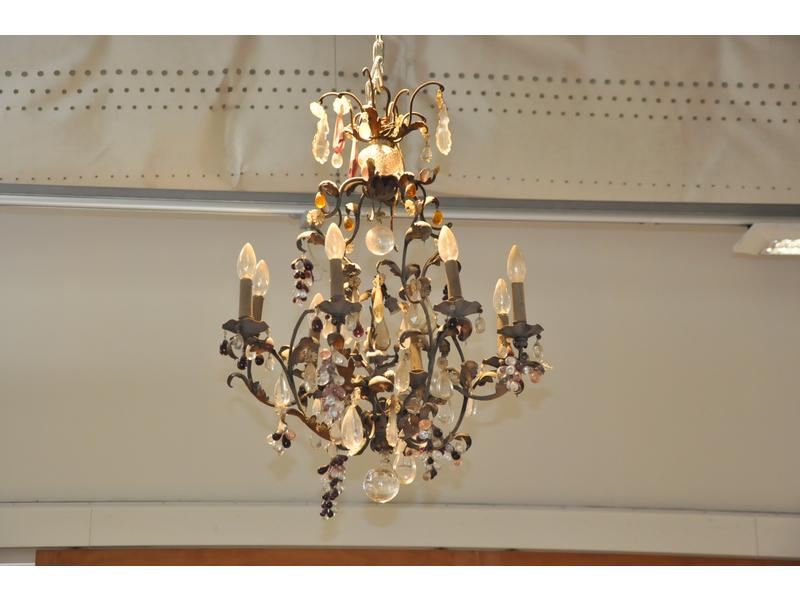 Lustre cage à huit bras de lumière en tôle et fer forgé à décor de feuillages et orné de pampilles en verre blanc et verre teinté en forme de poires et grains de raisin.  Fin XIXe siècle.  Hauteur : 80 cm.