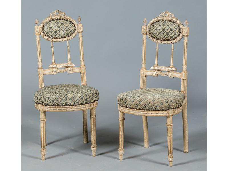 Paire de chaises volantes de style Louis XVI en bois sculpté et laqué blanc. Dossier médaillon orné de colonnes cannelées. Vers 1900. Garniture au point de croix.