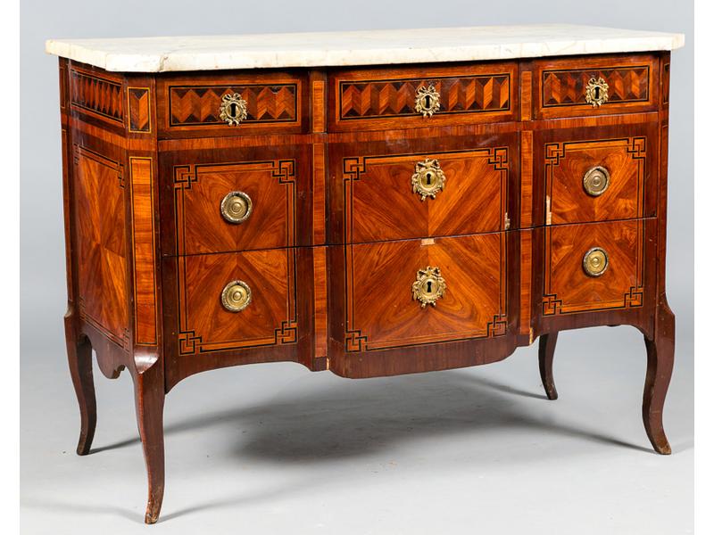 Commode rectangulaire à ressaut central en bois de placage en ailes de papillon dans des encadrements et filets à grecques.  Elle ouvre par trois tiroirs en ceinture et deux tiroirs principaux sans traverse.  Montants antérieurs à pans coupés reposant sur des pieds cambrés.  Plateau de marbre blanc.