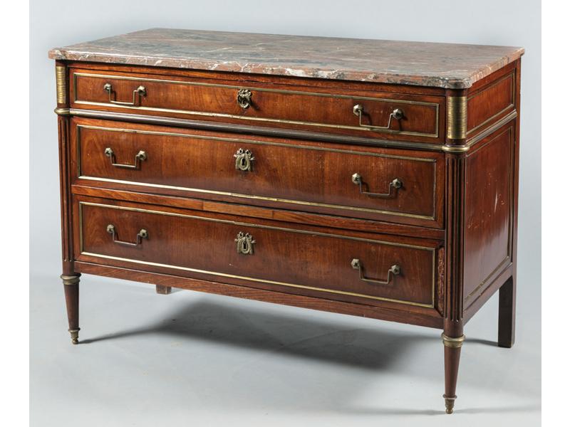 Commode rectangulaire Louis XVI en acajou et placage d'acajou ouvrant par trois tiroirs en façade. Montants arrondis à cannelures. Gratoirs, bagues et moulures en laiton.  Plateau de marbre gris veiné. Fin XVIIIe siècle. Dim.: 91x128x61 cm. Pieds et montants arrières d'époque postérieure. (manques)
