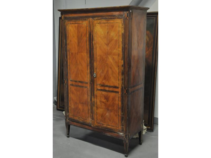 Petite armoire de style Louis XVI en bois marqueté ouvrant par deux portes.  Plateau de bois (rapporté) reposant sur des montants marquetés de fausses cannelures.  Epoque XIXe siècle.  Dim.: 163x97x45 cm. (chocs et vernis en mauvais état)