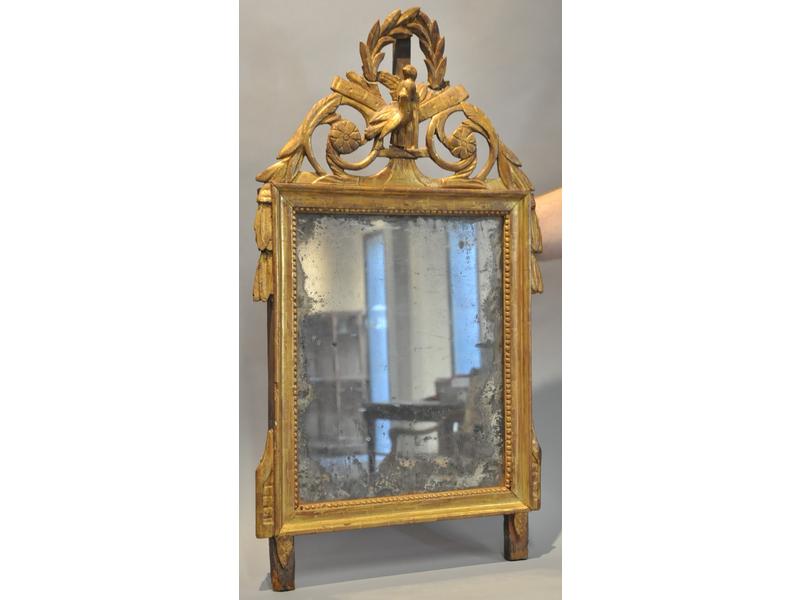 Petit miroir Louis XVI de forme rectangulaire dans un encadrement en bois doré à frise de perles.  Il est surmonté d'un fronton (en partie recollé) à motif de rinceaux, couronne de laurier et colombes.  Dim.: 80x45 cm.