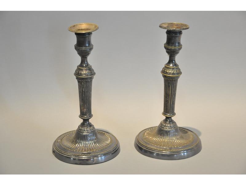 Paire de flambeaux en bronze argenté à décor de cannelures, feuilles d'eau et rang de perles.  Epoque Louis XVI.   Hauteur : 24.5 cm. (anciennement montés à l'électricité)
