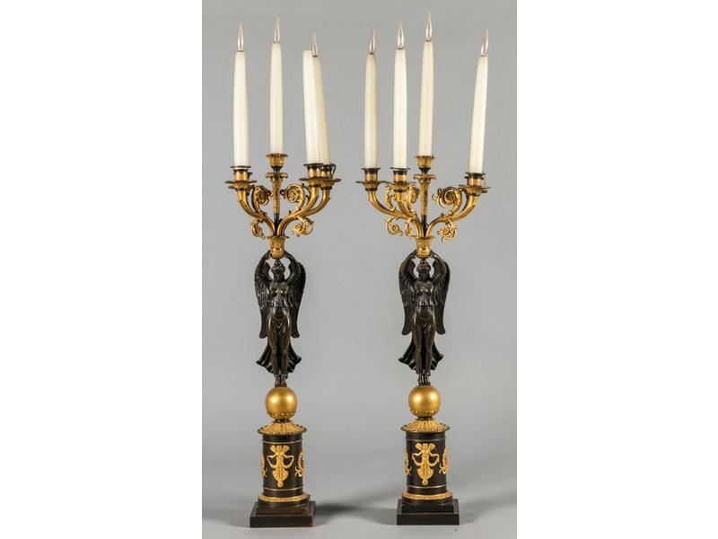 Paire de candélabres en bronze à double patine médaille et dorée, ornés de deux victoires ailées supportant cinq bras de lumière et reposant sur un socle à décor de déesse et couronne de laurier.  Epoque Empire.  Hauteur : 75 cm.  (électrifiés)