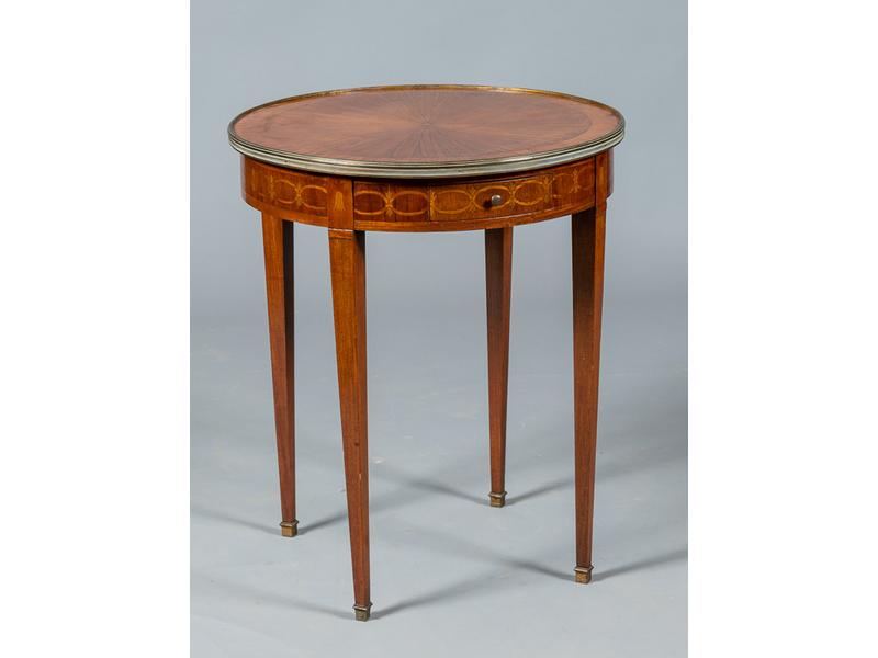Table de salon de style Directoire. Plateau circulaire marqueté d'un motif rayonnant à galerie de laiton. Ceinture ouvrant par un tiroir et reposant sur un trépied en gaine. Diamètre : 60 cm, hauteur : 72 cm.