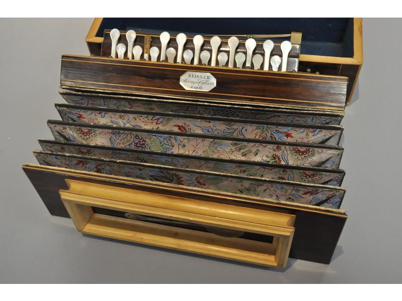 REISNER - 5 passage Colbert - Paris : Accordéon diatonique d'époque Charles X en placage de palissandre et bois clair. Le soufflet en toile et papier polychrome à décor floral (celui-ci en bon état). Touches en nacre (manque une). Dans son coffret d'origine en placage de palissandre (sans serrure, n