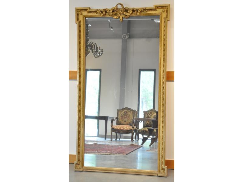 Grand miroir dans un encadrement en bois doré et redoré à grecques à décor sculpté d'un noeud de ruban, oves et raies de coeur.  Epoque Louis XVI.  Dim.: 177x101 cm.
