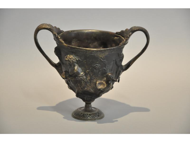 Coupe à anses en bronze de partine vert antique reposant sur un piédouche.  Panse ornée d'un centaure et personnages mythologiques.  Vers 1800.  Hauteur : 14.5 cm. Diamètre : 11.5 cm. (quelques usures à la patine)