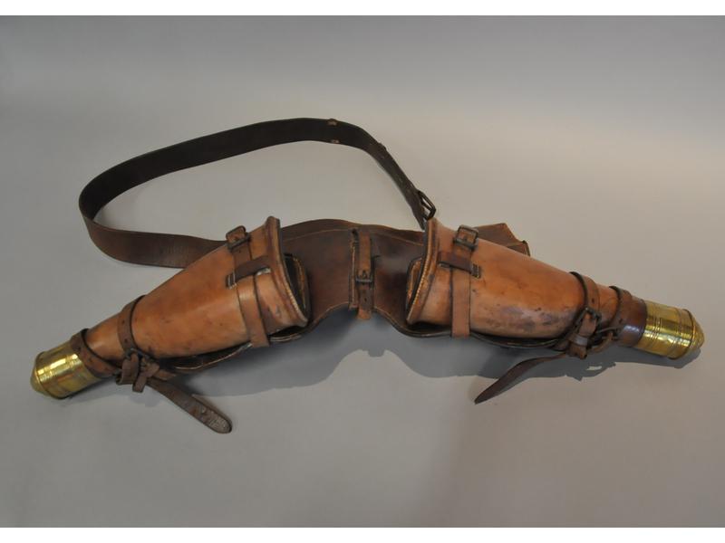 Paire de fontes de pistolets en cuir, destinées à être portées à l'encolure d'un cheval.  Les étuis sont ornés de deux embouts en laiton ciselé.  Epoque XIXe siècle.  Hauteur des étuis : 33 cm. (sangle droite cassée)
