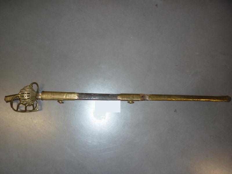 Sabre d'officier de cavalerie lourde. Poignée recouverte de basane avec filigrane. Monture en laiton, garde à coquille ajourée (accident au quillon). Lame à arrête médiane gravée, dorée et bleuie au tiers (restes). Fourreau en cuir à trois garnitures en laiton (fourreau en mauvais état, non d'origin