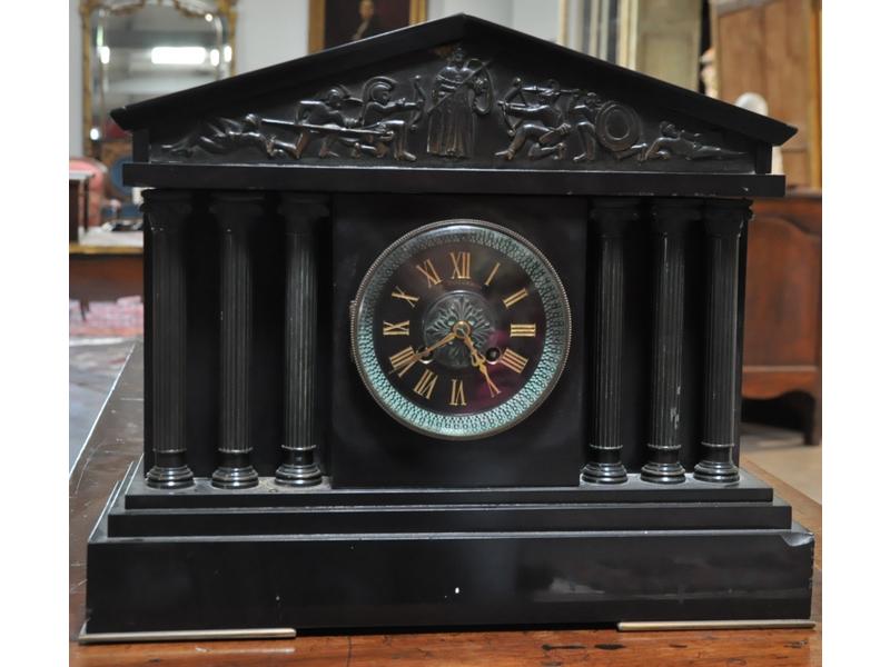 Pendule en marbre noir et laiton en forme de temple grec.  Cadran signé DUCOMMUN, flanqué de trois colonnes à chapiteaux de part et d'autre et surmonté d'une frise représentant une allégorie de la guerre (Mars).  Dim.: 34x40x16 cm.